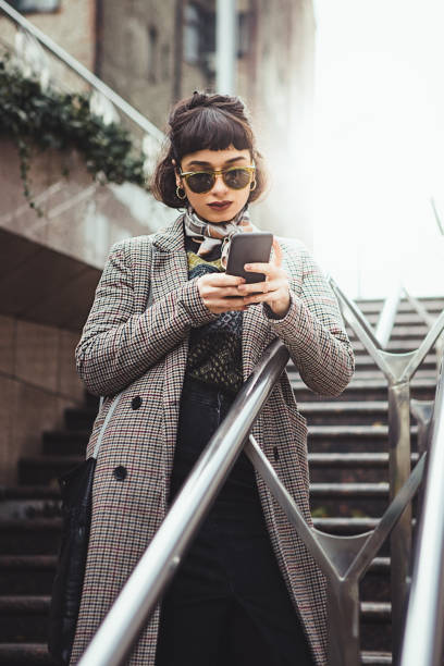 winter portrait of a young woman in the city texting - fashion stock pictures, royalty-free photos & images