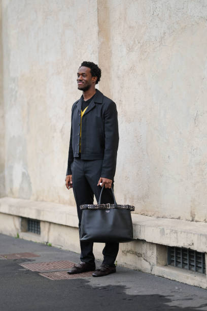 Wisdom Kaye wears black and yellow Prada sweater, black cropped jacket, black Prada slim fit trouser pants, shiny dark brown tassel loafer leather...