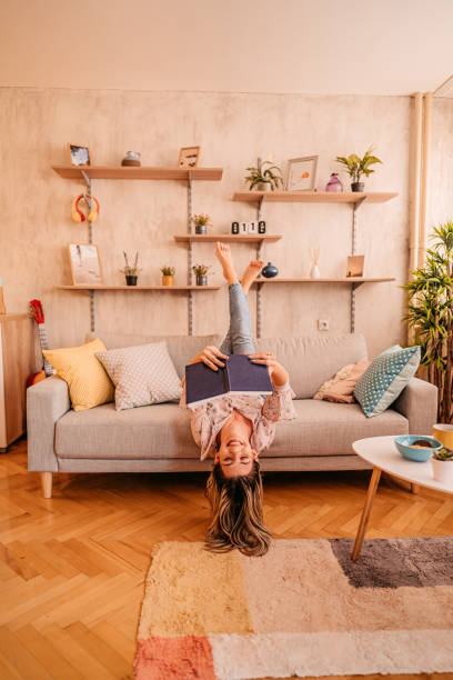 woman at home lying on sofa and reading book - home decoration stock pictures, royalty-free photos & images