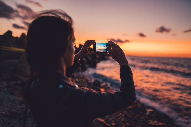 woman at the beach photographing the sunset - travel stock pictures, royalty-free photos & images