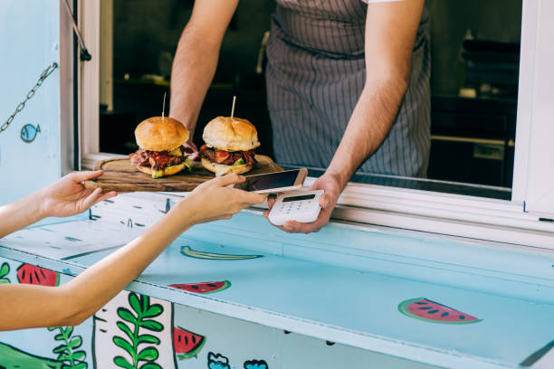 woman buying burgers from food van and using smartphone. - junk food stock pictures, royalty-free photos & images