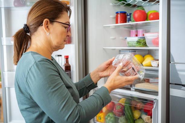 woman by the fridge reading label of refrigerated food package - food stock pictures, royalty-free photos & images