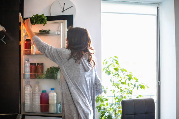 woman by the open fridge taking a bunch of parsley - food stock pictures, royalty-free photos & images