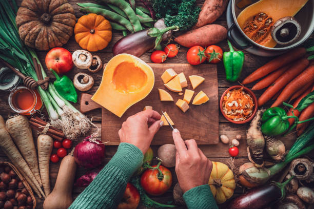 woman chopping squash on a table full of fresh autumnal vegetables - food stock pictures, royalty-free photos & images