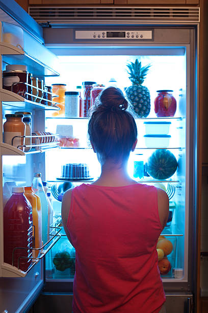 woman contemplating midnight snack late night with open refrigerator - food stock pictures, royalty-free photos & images