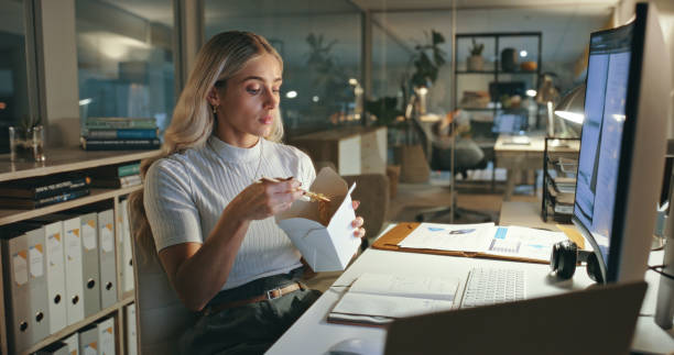 woman, eating and chinese food in office at night, working or employee reading computer, research and planning project. person, thinking and hungry for asian dinner and takeaway on desk in workplace - junk food stock pictures