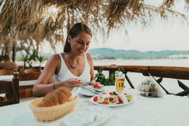 woman eating greek salad in a restaurant at the seaside in greece - food stock pictures, royalty-free photos & images