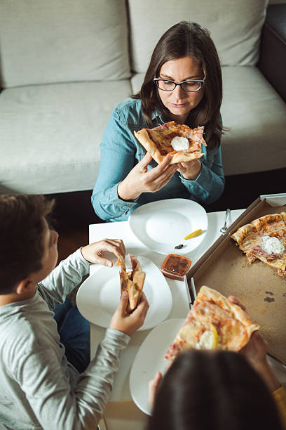 woman eating pizza with family - junk food stock pictures, royalty-free photos & images