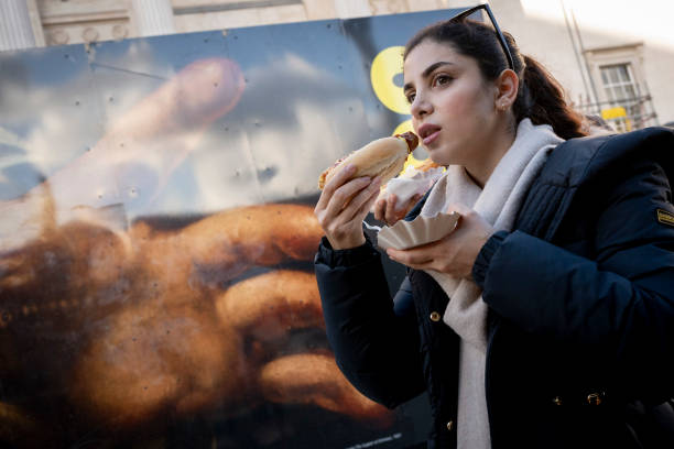Woman eats a sausage while walking past a large detail reproduction of Caravaggio's 'The Supper of Emmaus' outside the National Gallery that is in...