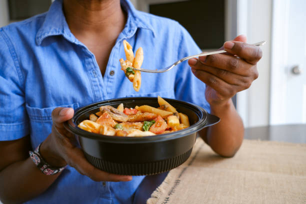 woman eats takeout pasta and chicken dish - junk food stock pictures, royalty-free photos & images