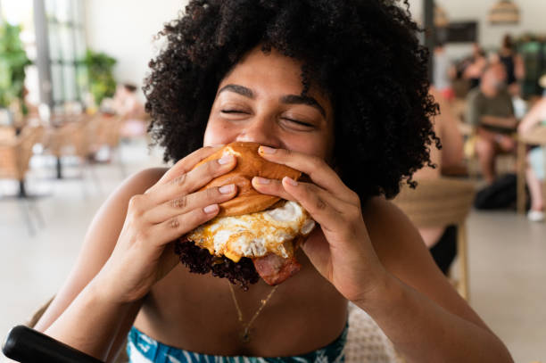 woman enjoying a delicious burger in a restaurant - junk food stock pictures, royalty-free photos & images