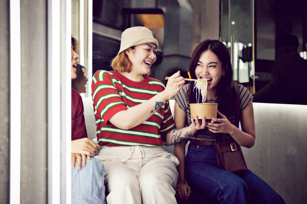 woman feeding noodles to female friend - junk food stock pictures, royalty-free photos & images