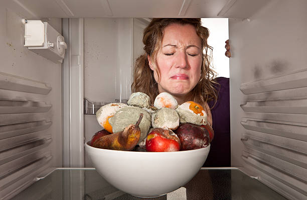woman finds bowl of rotting fruit in the fridge. - food stockfoto's en -beelden