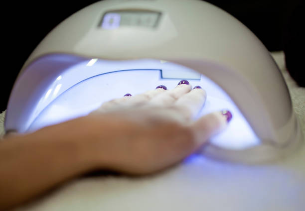 woman fliling nails with uv lamp in background. - nails art stock pictures, royalty-free photos & images
