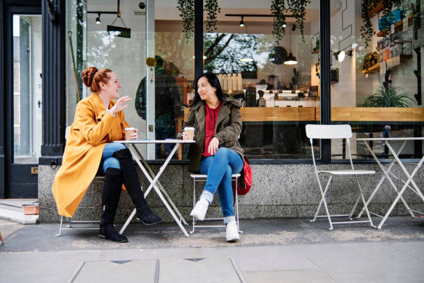 woman gesturing while talking with female friend outside coffee shop - coffee stockfoto's en -beelden