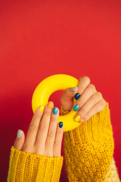 woman hands with bright manicure and in yellow knitted sweater are holding illuminating yellow bagel against red background. trendy colors of the year 2021. front view. copy space for your design - nails art stock pictures, r