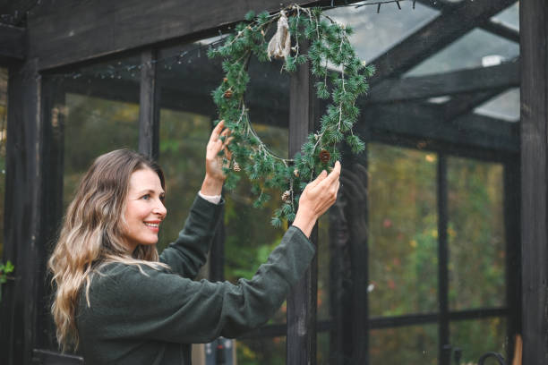 woman hangs a christmas wreath - garden decoration stock pictures, royalty-free photos & images