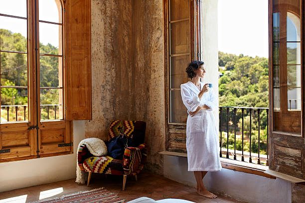 woman having coffee while standing at window - travel stockfoto's en -beelden