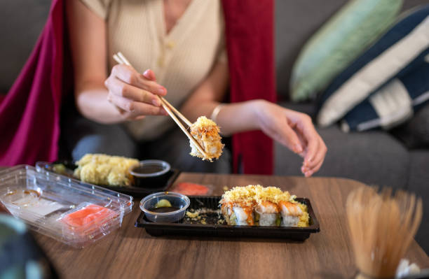 woman having takeaway or delivery sushi rolls meal from a plastic package with sauces at home - junk food stock pictures, royalty-free photos & images