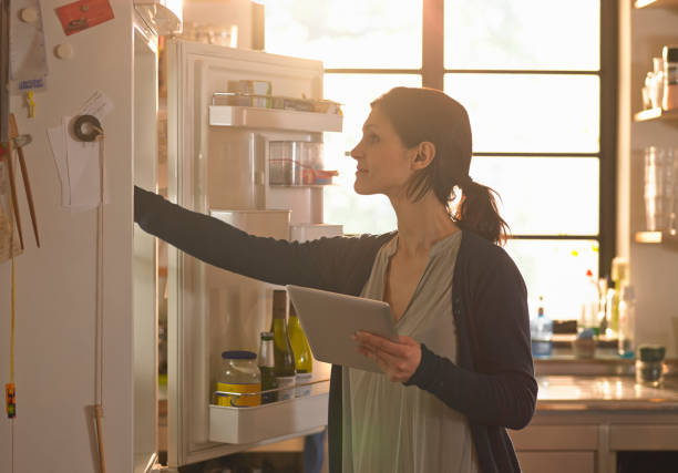 woman holding an tablet computer whilst looking in the fridge - home decoration stock pictures, royalty-free photos & images