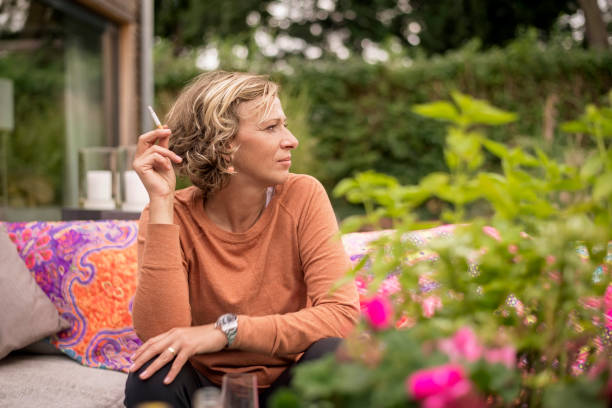 woman holding cigarette while sitting on sofa at backyard - garden decoration photos et images de collection