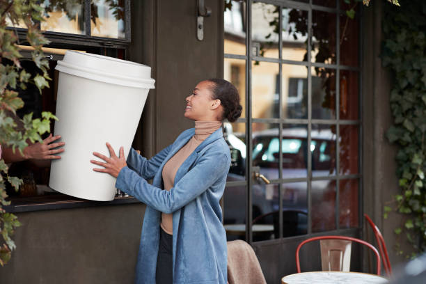 woman holding large disposable coffee cup at take away counter of cafe - junk food stock pictures, royalty-free photos & images