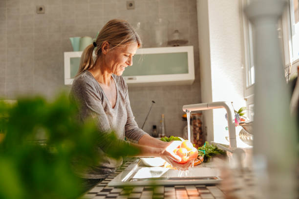 woman in kitchen washing tomatoes - food stock pictures, royalty-free photos & images