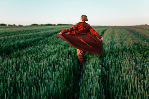 woman in red coat walking in the field at sunset - fashion stock pictures, royalty-free photos & images