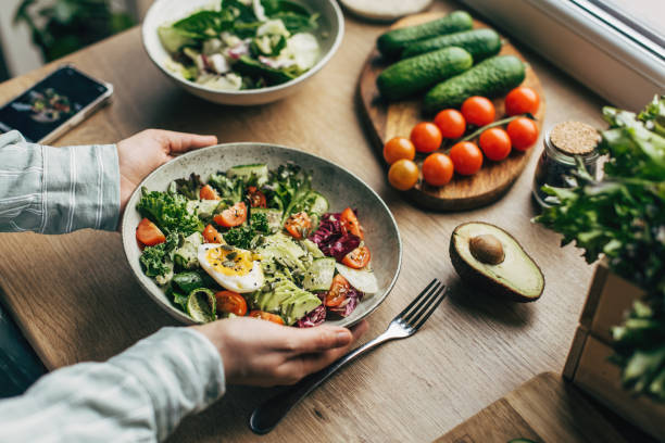 woman mixing delicious superfood salad ingredients with wooden spoons in kitchen - food stock pictures, royalty-free photos & images
