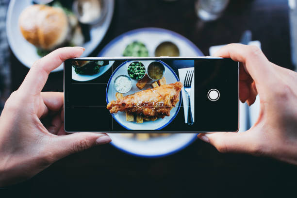 woman photographing fish and chips in a restaurant with a smartphone - food stock pictures, royalty-free photos & images