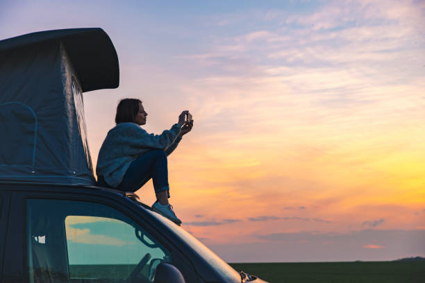woman photographing the sunset from the rood of her campervan - travel stock pictures, royalty-free photos & images