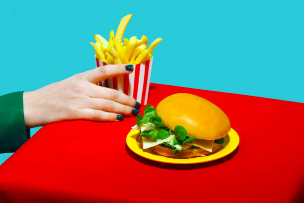woman picking up french fries near burger on table against blue background - junk food stock pictures, royalty-free photos & images