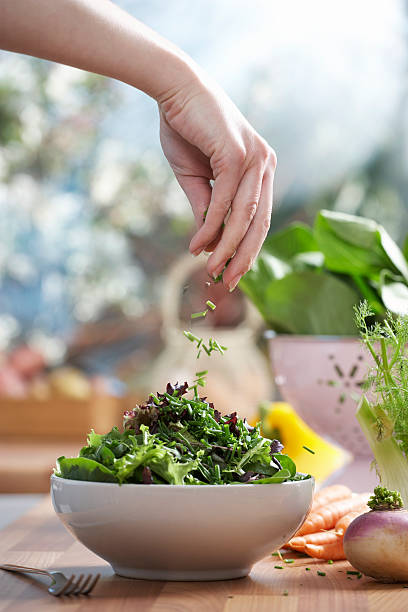 woman pouring herbs into bowl of salad in kitchen, close-up of hand - food stock pictures, royalty-free photos & images