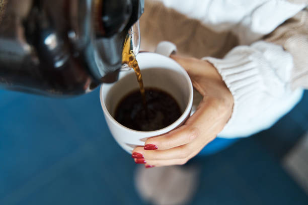 woman pouring herself hot coffee to a mug. - coffee stock pictures, royalty-free photos & images