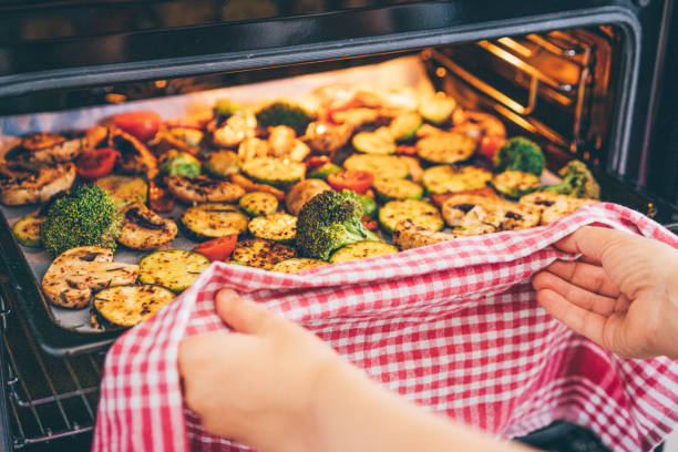 woman putting a tray of vegetables in the oven. - food stock pictures, royalty-free photos & images