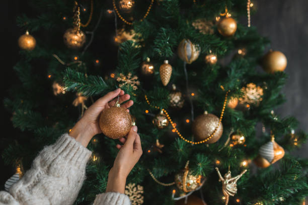 woman putting on christmas tree golden ornaments. - home decoration stock pictures, royalty-free photos & images