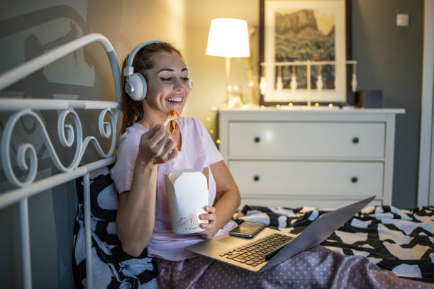 woman relaxing in bed and eating pasta - junk food stock pictures, royalty-free photos & images