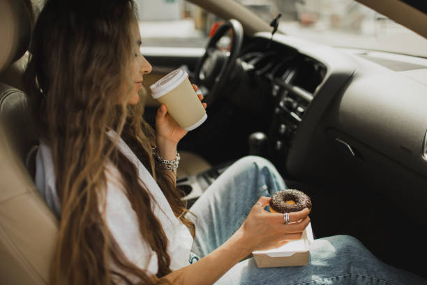 woman relaxing in car and enjoying coffee with donut. fast food in road trip. - junk food stock pictures, royalty-free photos & images