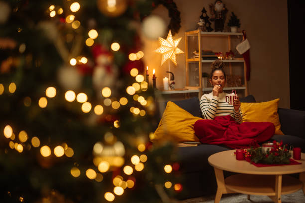 woman relaxing on sofa eating christmas candy cane at home - home decoration stock pictures, royalty-free photos & images