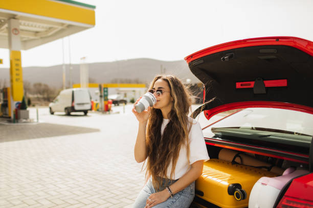 woman relaxing with coffee on the road trip. coffee break on gas station, sitting on car boot. - junk food stock pictures, royalty-free photos & images
