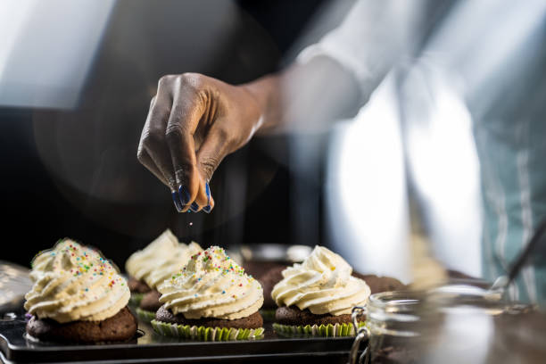 woman's hand sprinkling hundreds and thousands on cupcake - home decoration stock pictures, royalty-free photos & images