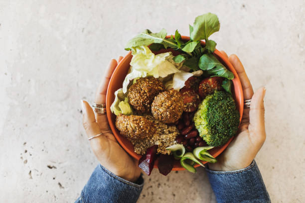 woman's hands holding bowl with falafel, broccoli, greens, cherry tomatoes, red beans, beetroot and quinoa - junk food stock pictures, royalty-free photos & images
