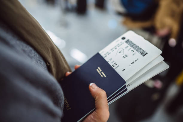 woman’s hands holding passports & boarding passes of her family while waiting at the check-in counter in the airport - travel stock pictures, royalty-free photos & images