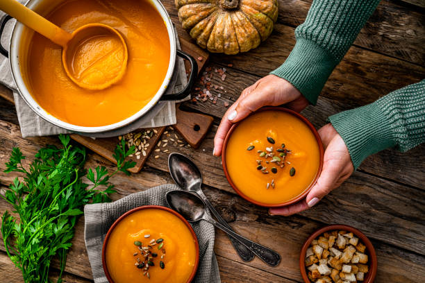 woman serving two bowls of pumpkin soup for thanksgiving meal - food stock pictures, royalty-free photos & images