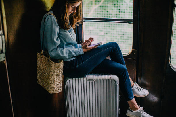 woman sitting on suitcase in train looking at smart phone - travel stock pictures, royalty-free photos & images