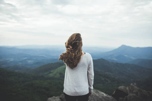 woman stares out at a beautiful mountain scene - fashion stock-fotos und bilder