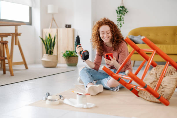 woman using a mobile phone while renovating and repairing an old chair. - home decoration stock pictures, royalty-free photos & images