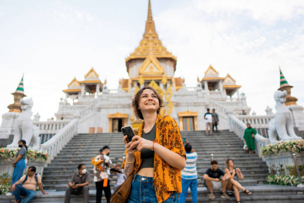 woman using smartphone standing on the background of wat traimit - travel stock pictures, royalty-free photos & images