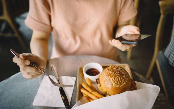 woman using smartphone while having meal in a restaurant - junk food stock pictures, royalty-free photos & images
