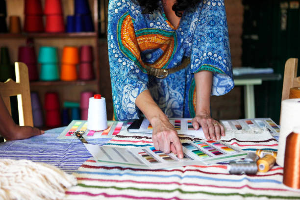 woman wearing a caftan pointing at a color card on a table of textiles - fashion photos et images de collection